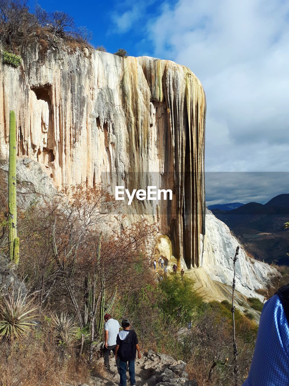 REAR VIEW OF PEOPLE ON ROCK AGAINST MOUNTAIN