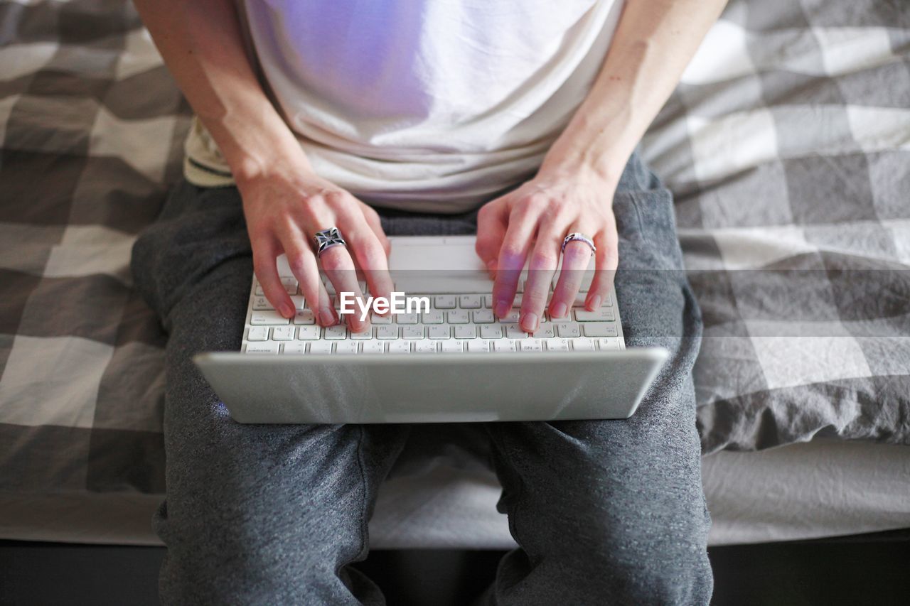 Midsection of man using laptop while sitting on bed at home