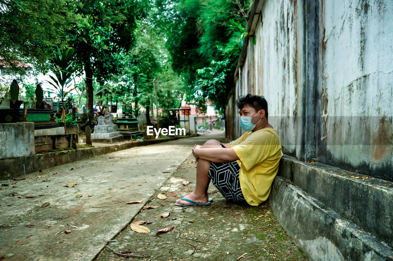 Side view of young man sitting on plants