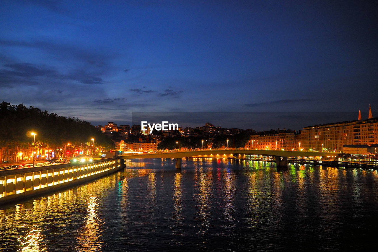 RIVER BY ILLUMINATED CITY AGAINST SKY AT NIGHT