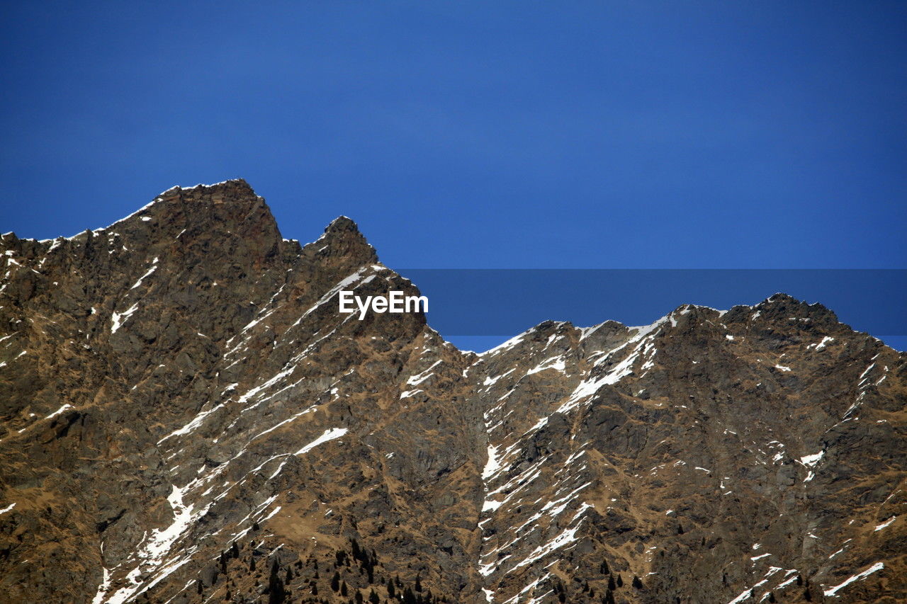 mountain, sky, scenics - nature, nature, environment, mountain range, landscape, beauty in nature, snow, cold temperature, winter, mountain peak, blue, rock, summit, ridge, no people, clear sky, travel destinations, land, travel, wilderness, outdoors, activity, snowcapped mountain, tranquility, extreme terrain, non-urban scene, day, leisure activity, cloud, tranquil scene, high up, tourism, sunny, adventure, plateau