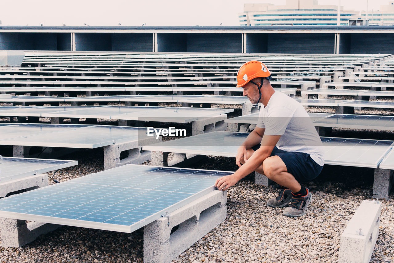 Serious male in helmet worker installing modern solar panels while working in industrial area of plant on sunny day