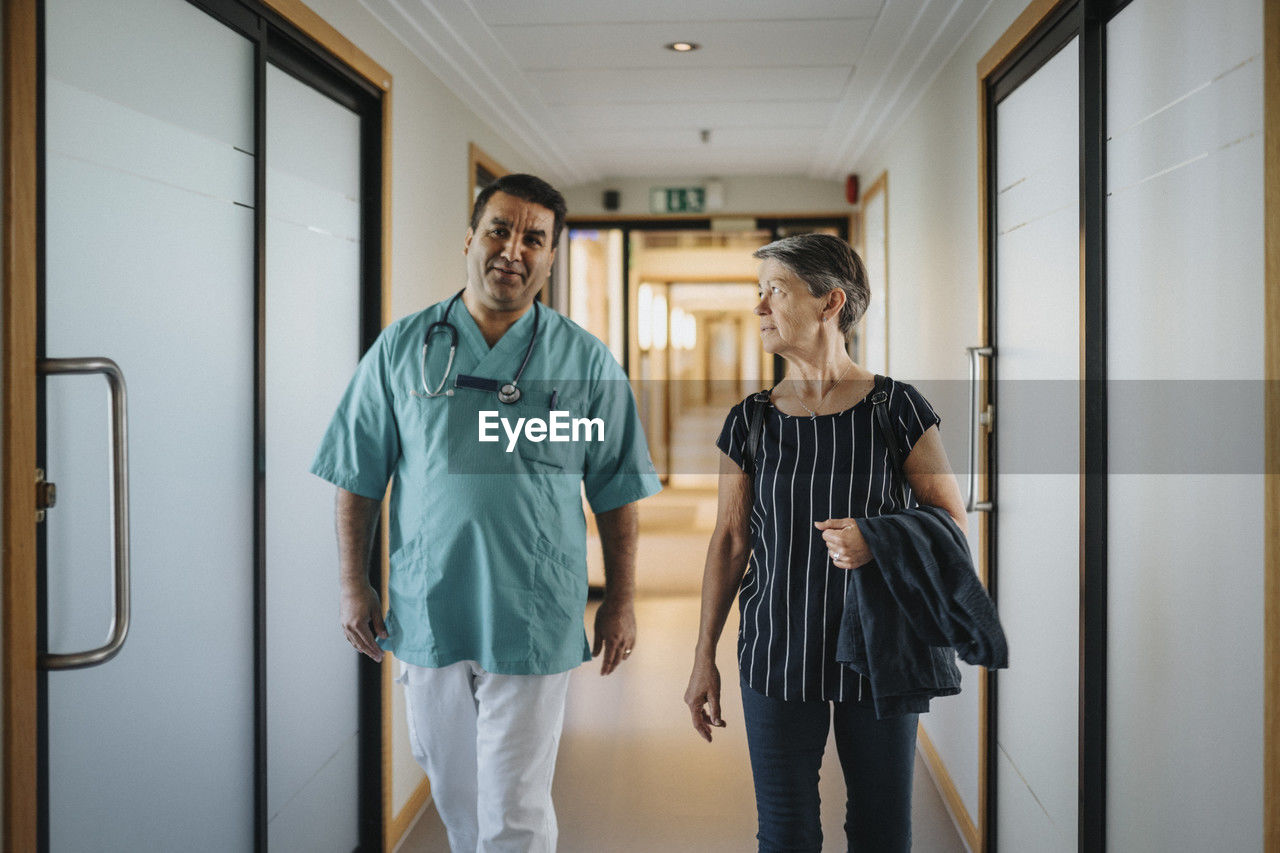 Doctor discussing with senior patient while walking in corridor of hospital