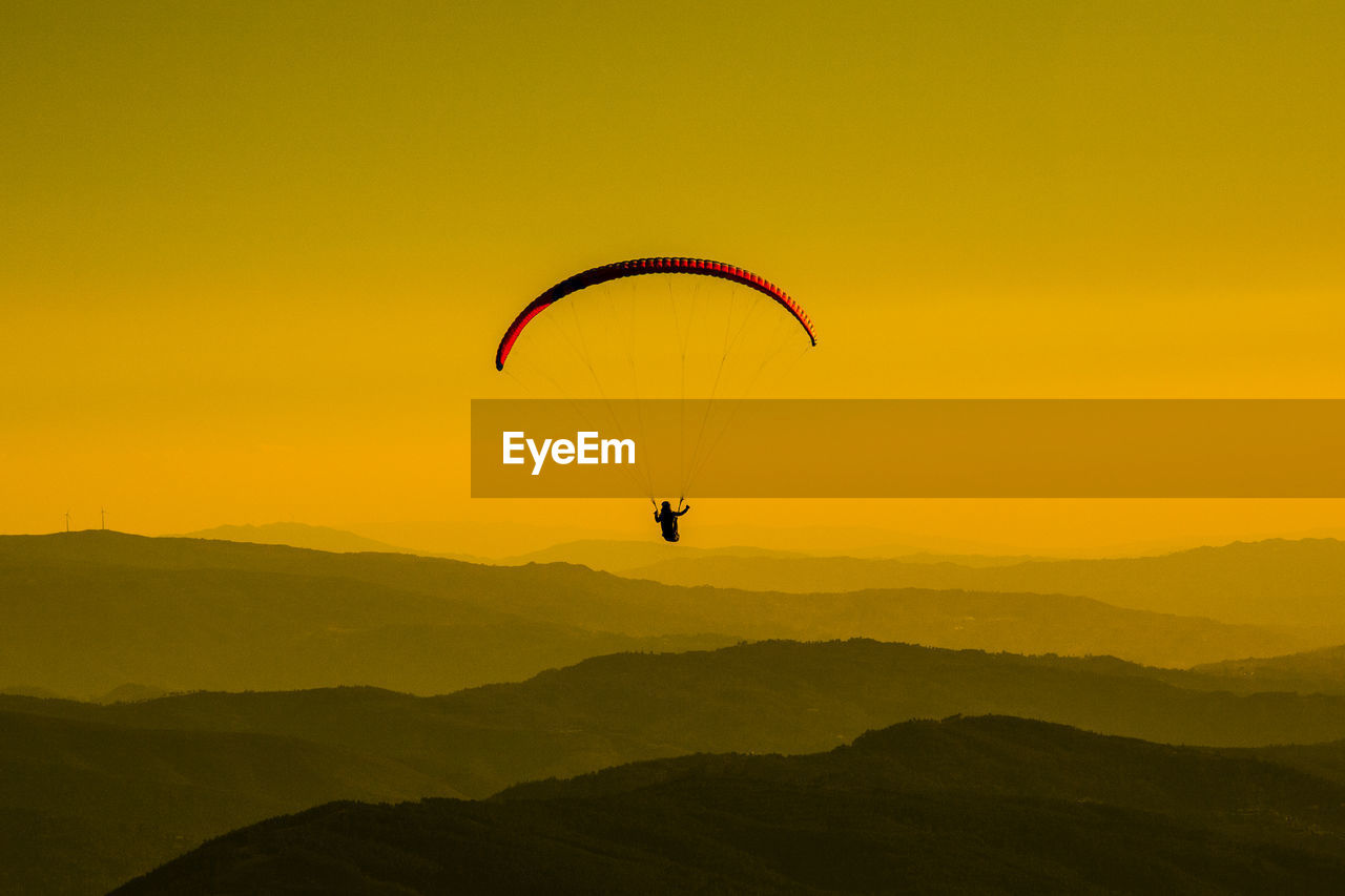 Silhouette person paragliding against sky during sunset