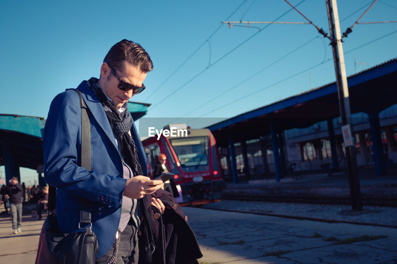 Handsome man using phone at railroad station platform