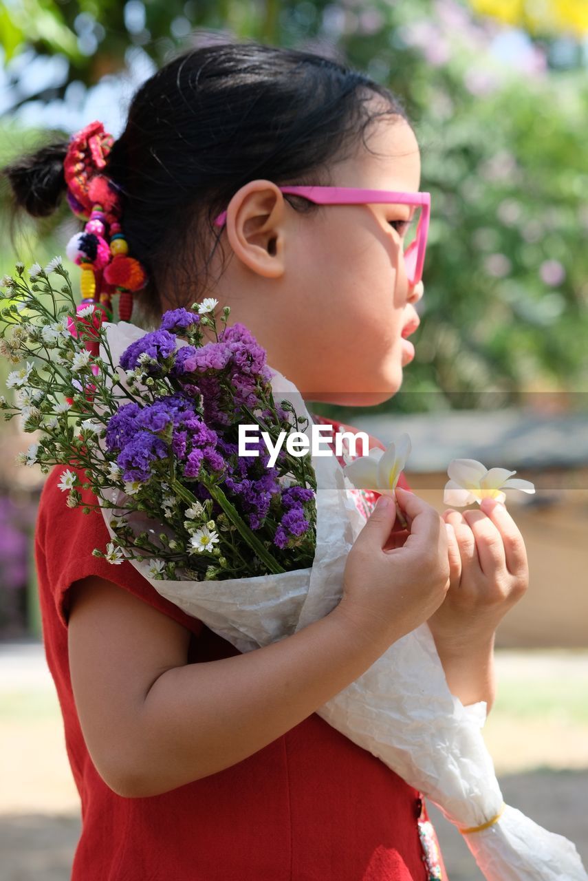 Cute girl holding bouquet while standing outdoors