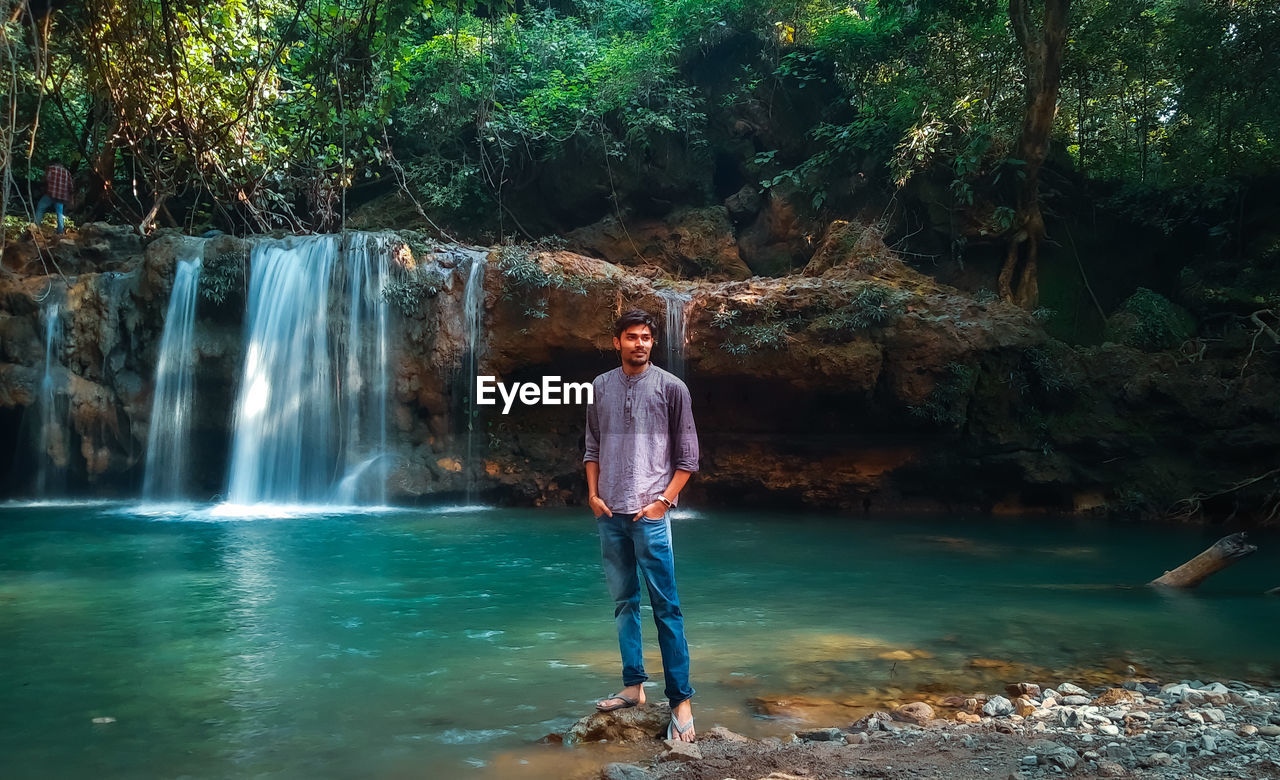 FULL LENGTH OF MAN STANDING BY WATERFALL