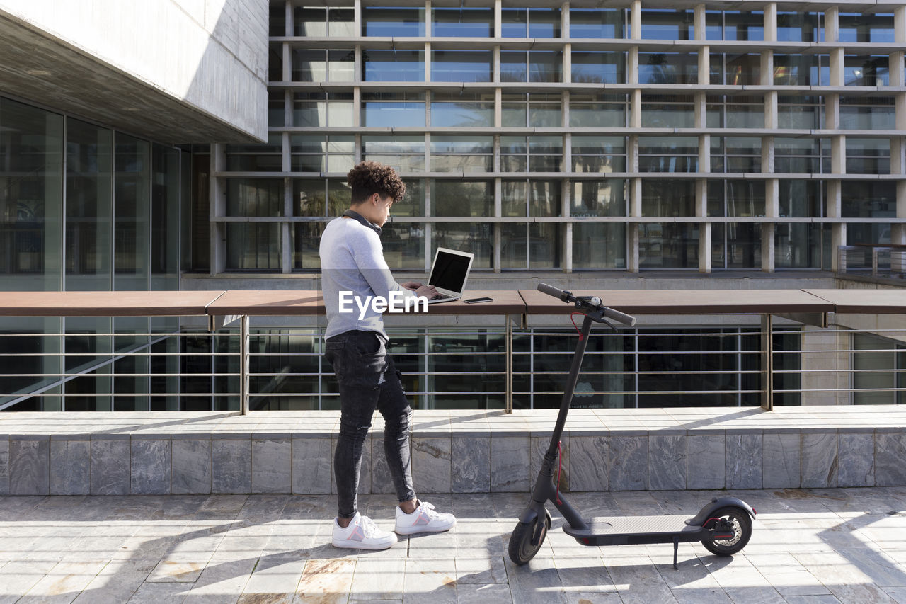 Young man with e-scooter using laptop in the city