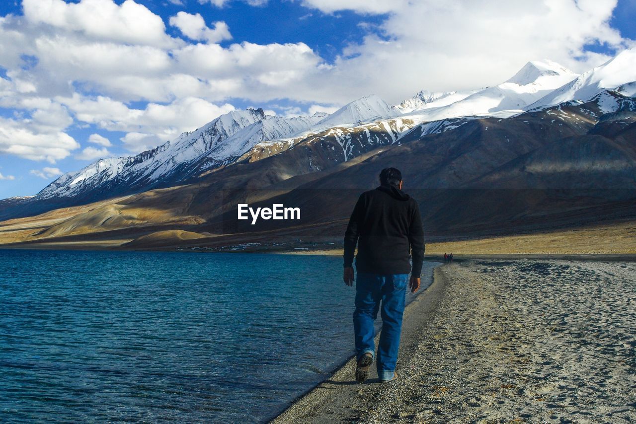 Rear view of man walking by pangong tso by mountains against sky