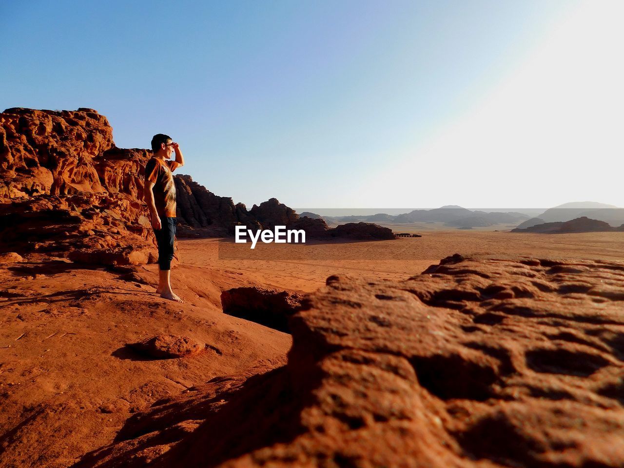 Side view of man standing on rock against sky