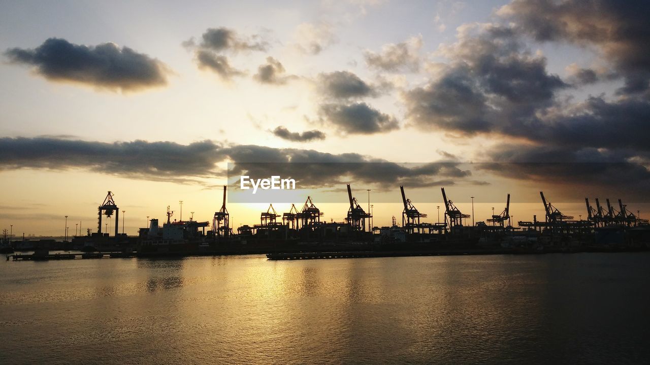 Sea by silhouette commercial dock against sky during sunset