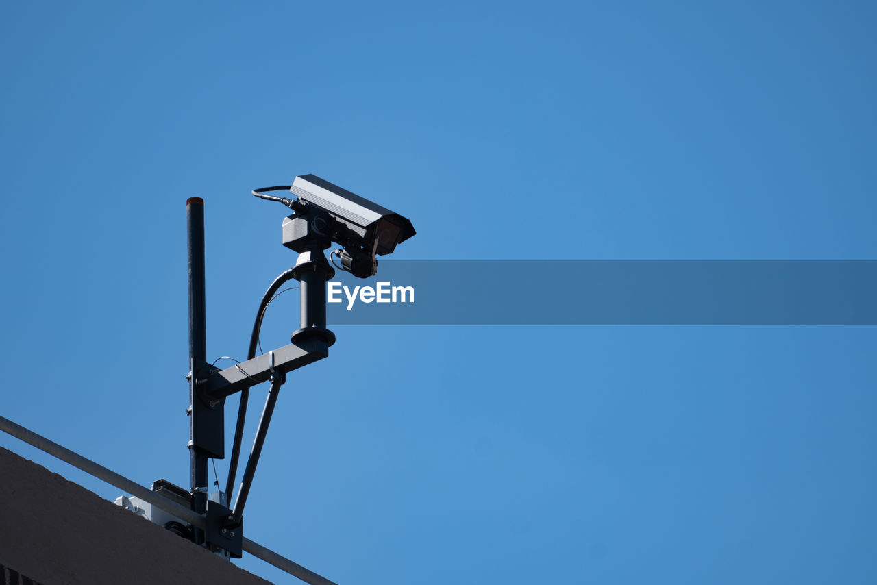 Low angle view of security camera against clear blue sky