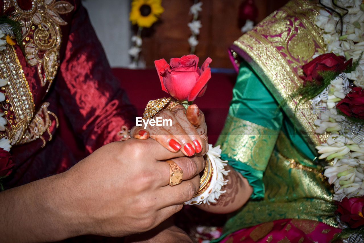 MIDSECTION OF COUPLE HOLDING HANDS IN TRADITIONAL DRESS