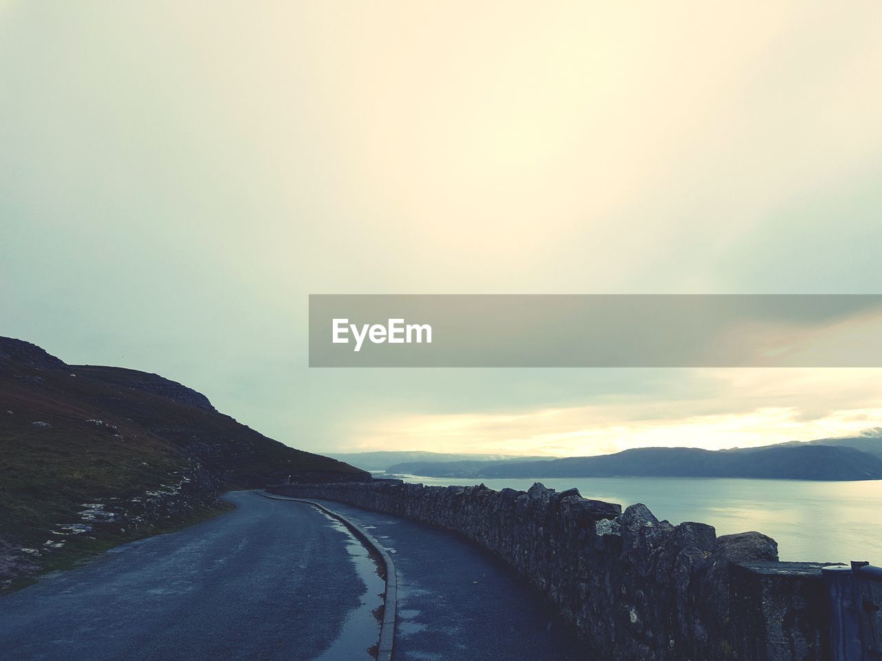 Road by mountains against sky during sunset