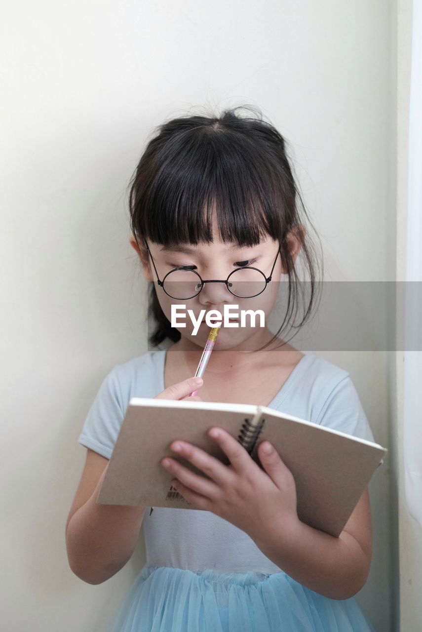 A child with glasses holding a pencil and write in the notebook intently. 