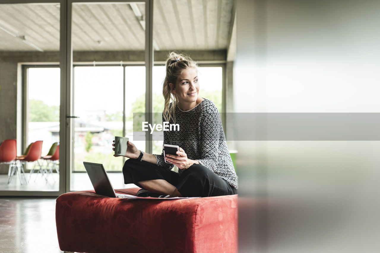 Young businesswoman working in modern office, sitting on stool, using laptop