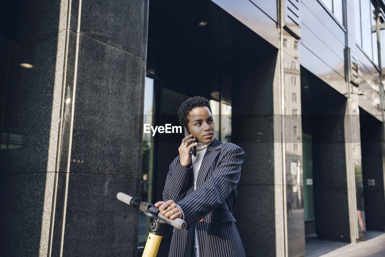 Young businesswoman with electric push scooter looking away while talking through mobile phone