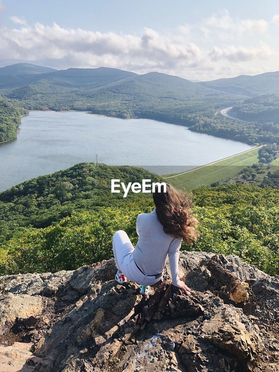 Rear view of woman crouching on cliff against lake