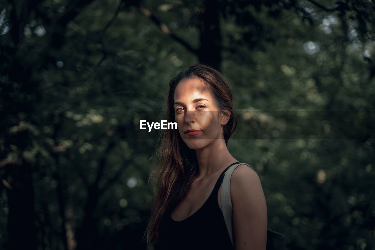 Portrait of young woman standing against trees