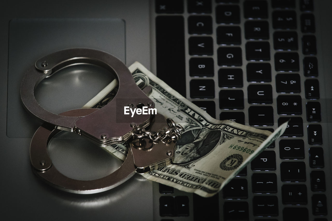 High angle view of handcuffs and us currency on laptop