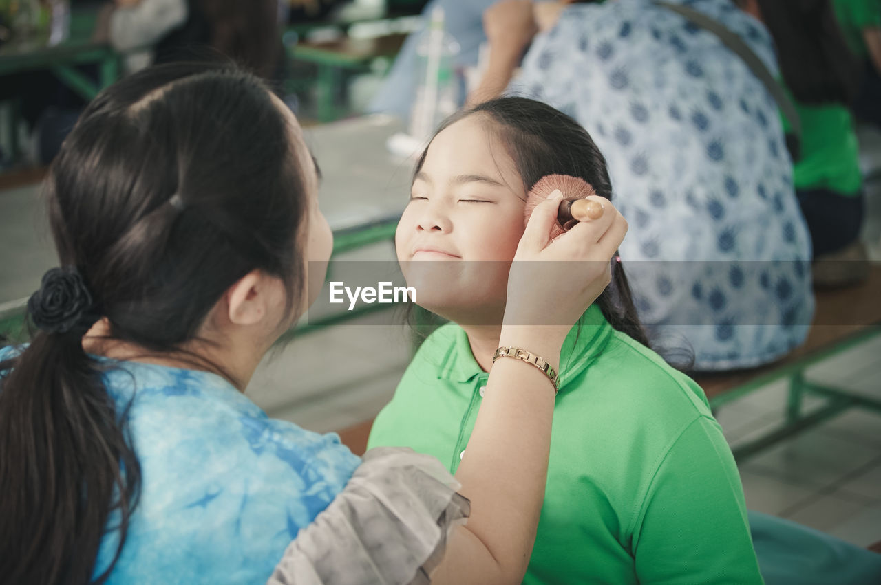 Mother applying make-up of daughter with brush