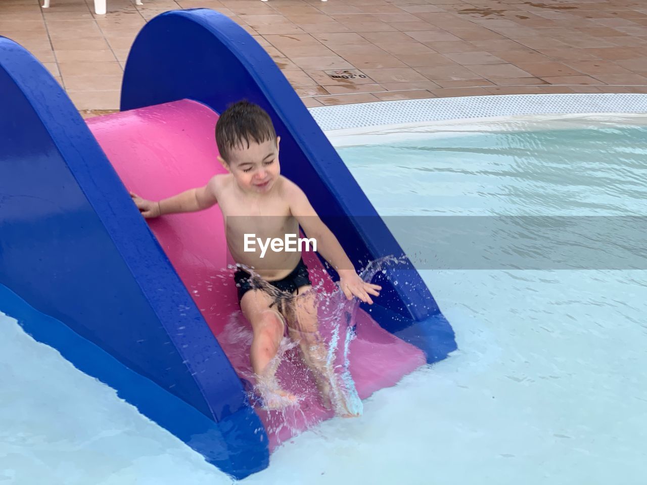 High angle view of shirtless boy sliding in swimming pool