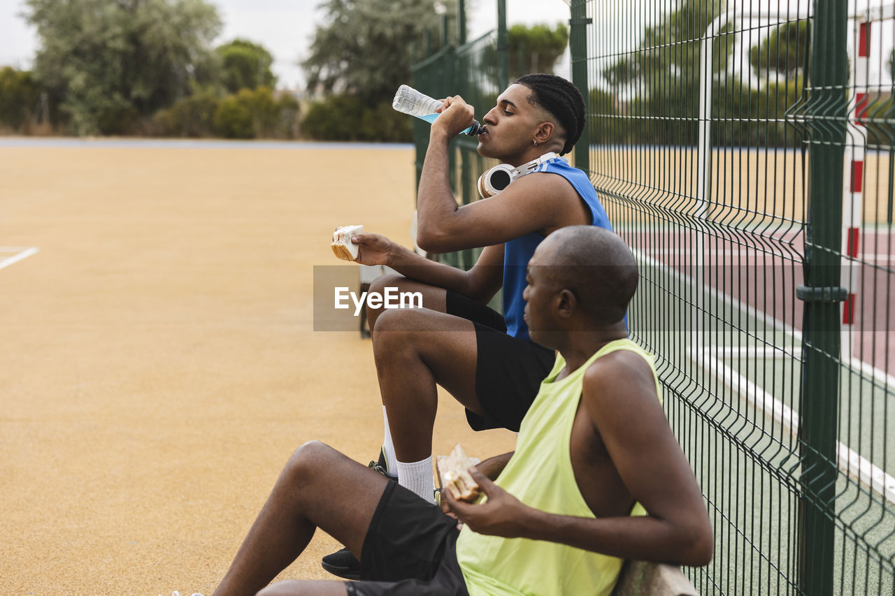 Young man drinking sports drink sitting by father on bench