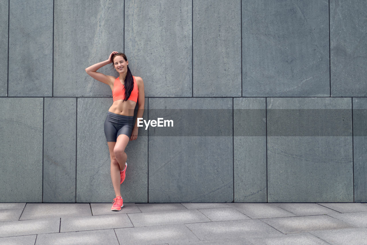 Woman in sports clothing standing against wall