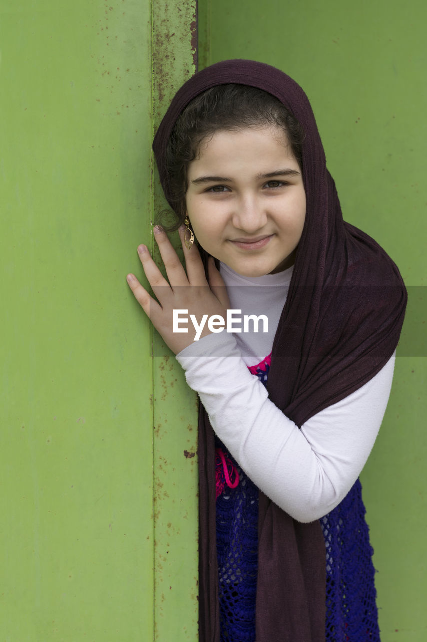 PORTRAIT OF HAPPY YOUNG WOMAN STANDING AGAINST WALL