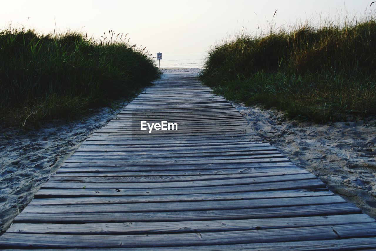 Walkway leading towards beach against clear sky