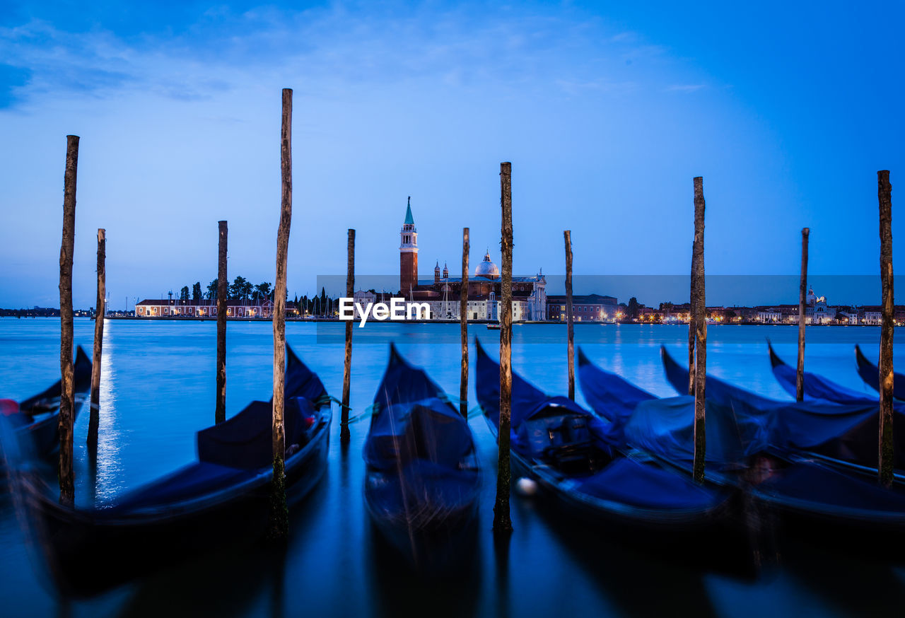 Gondolas moored by wooden post at harbor against sky at dusk