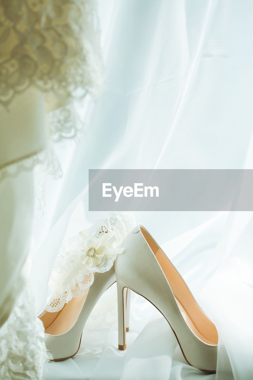 Composition of high heeled beige shoes placed on bridal veil