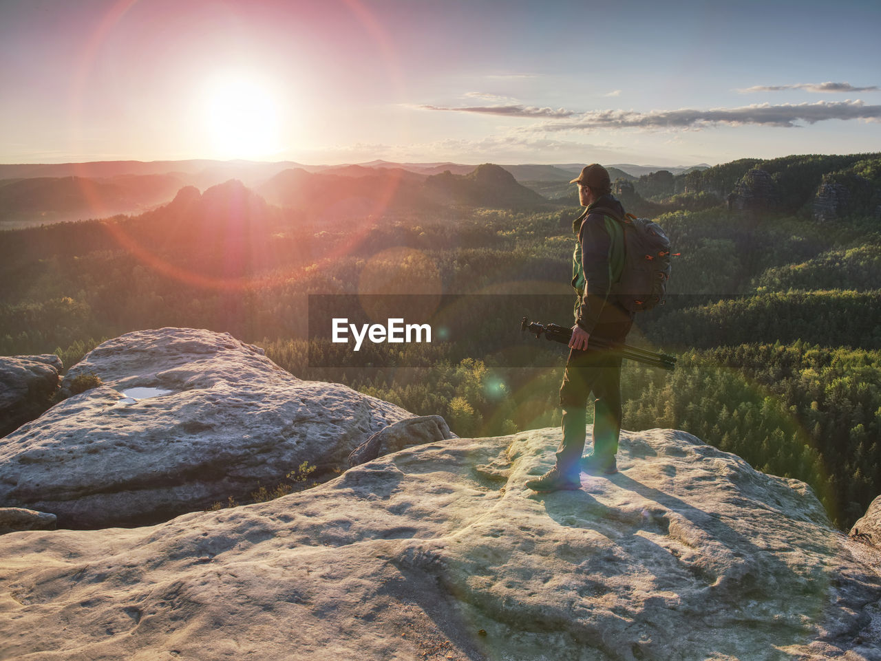 Photographer on mountain cliff above valley hold tripod. hiker take picture with camera in hands