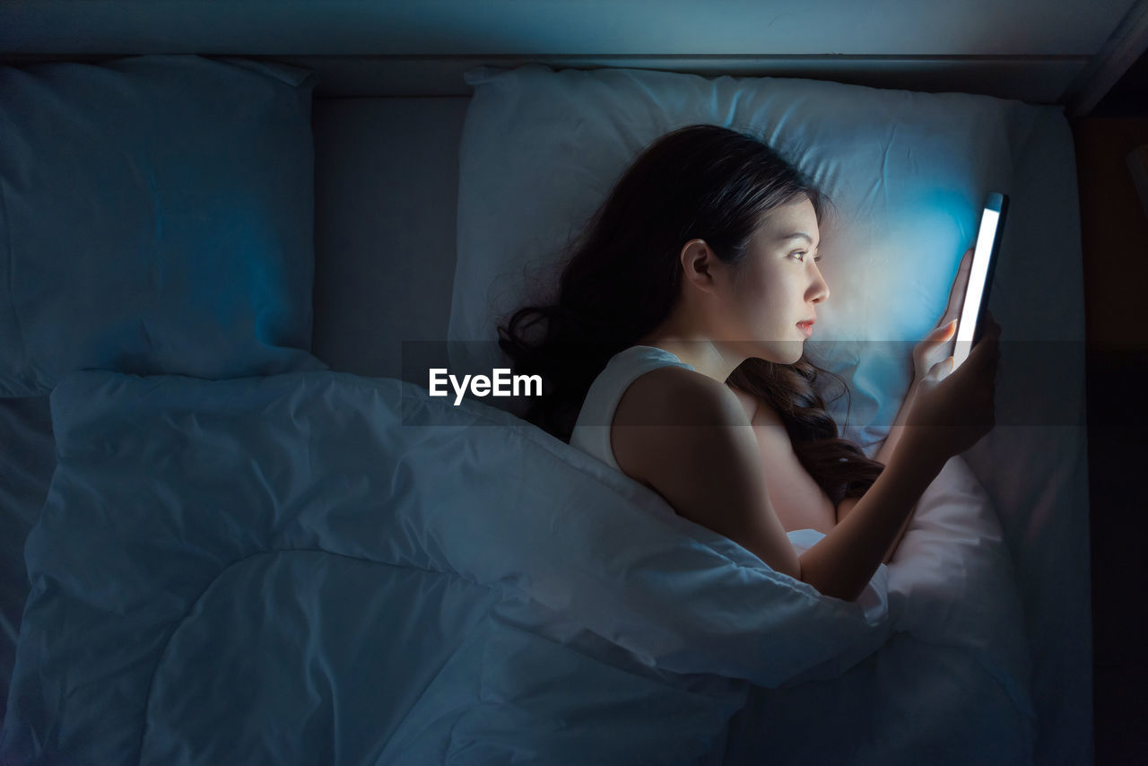 Young woman using mobile phone while sitting in bed