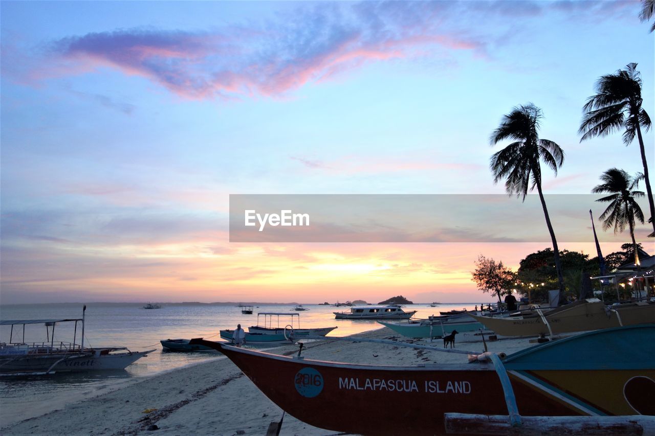 BOATS MOORED ON BEACH AGAINST SKY DURING SUNSET