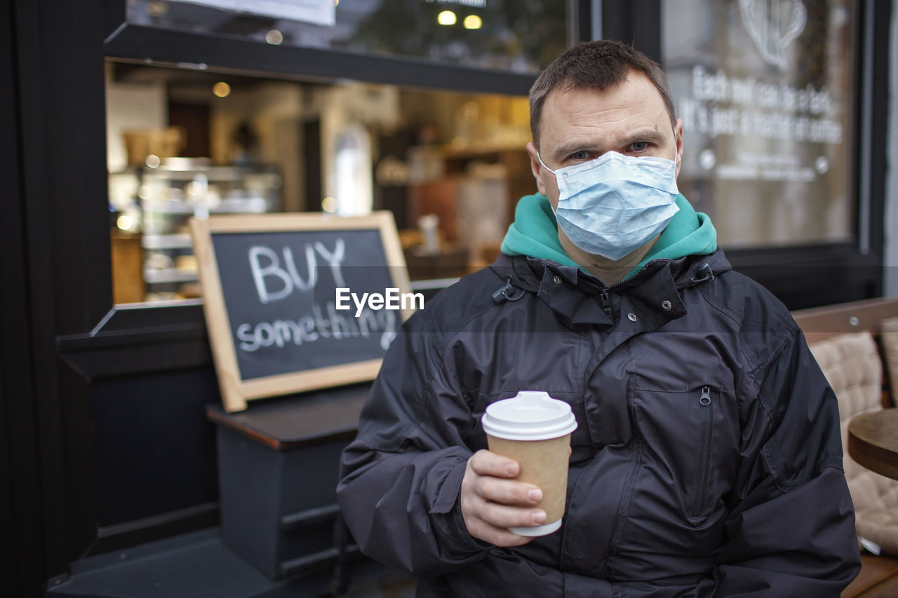 Portrait of man wearing mask holding coffee cup standing outdoors