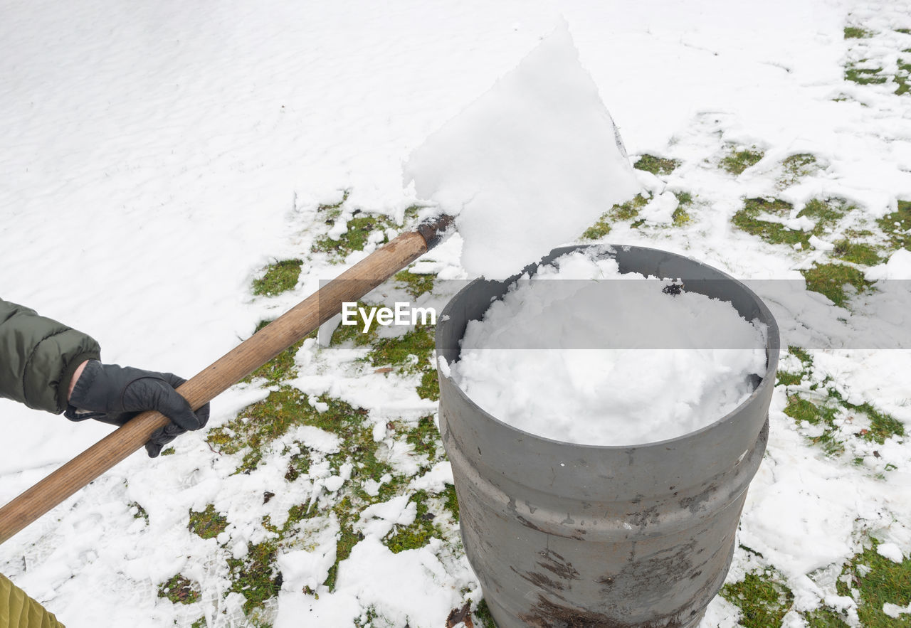 Middle-aged woman is collecting snow in a barrel with a shovel,natural resources