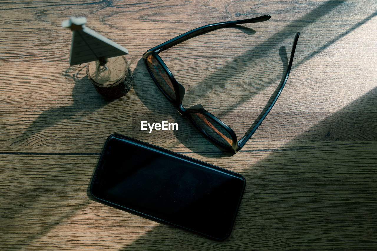 Directly above shot of sunglasses with smart phone and christmas model on wooden table