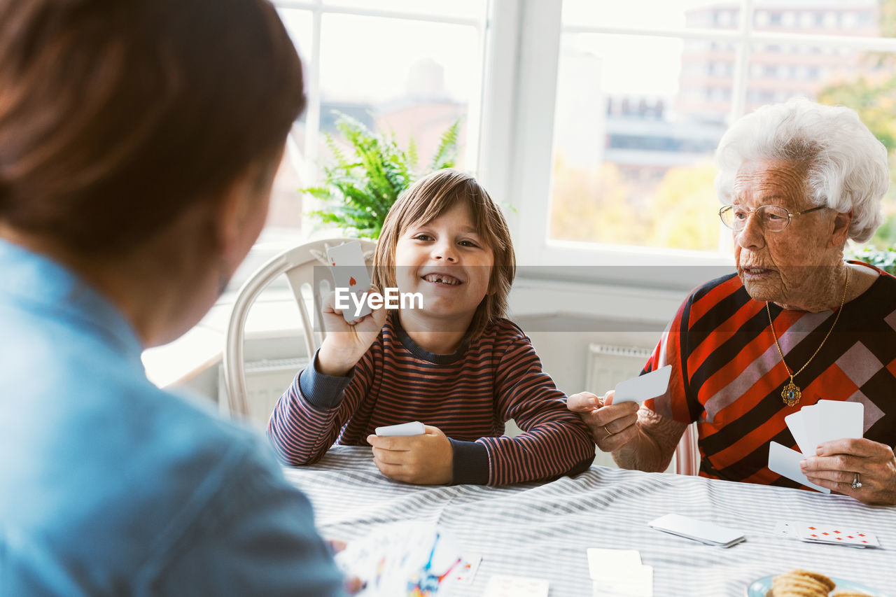 Happy boy playing cards with mother and great grandmother at home