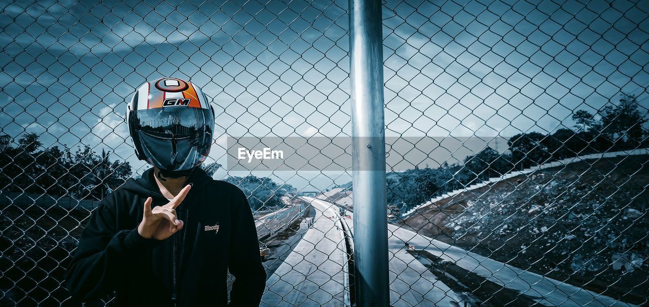 MAN LOOKING THROUGH CHAINLINK FENCE