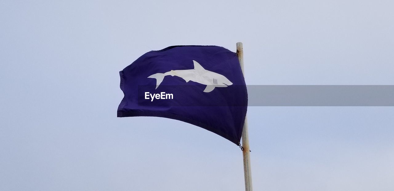 Low angle view of flag waving against clear blue sky