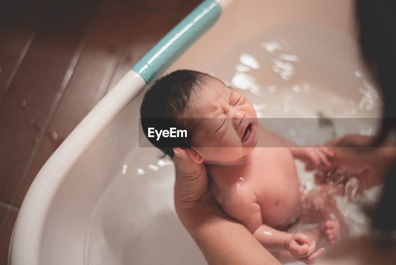 Cropped hands of mother bathing cute daughter in bath tub at home