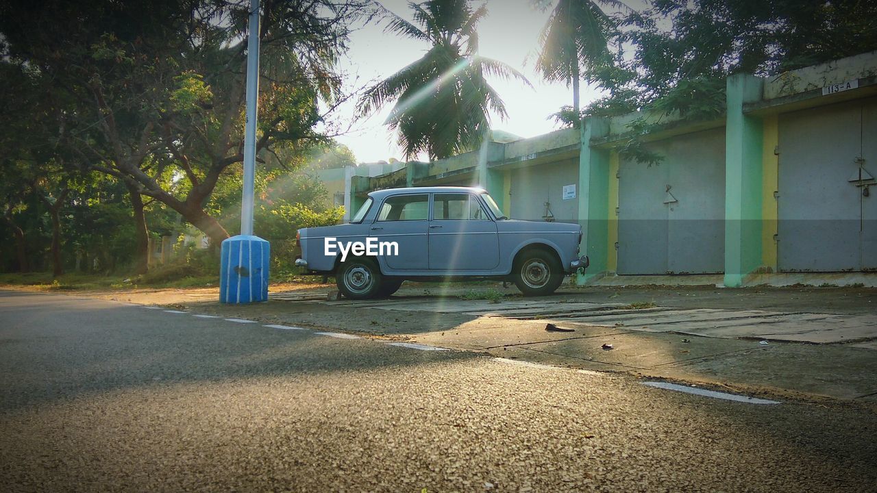 Vintage car parked by building on street against trees during sunny day