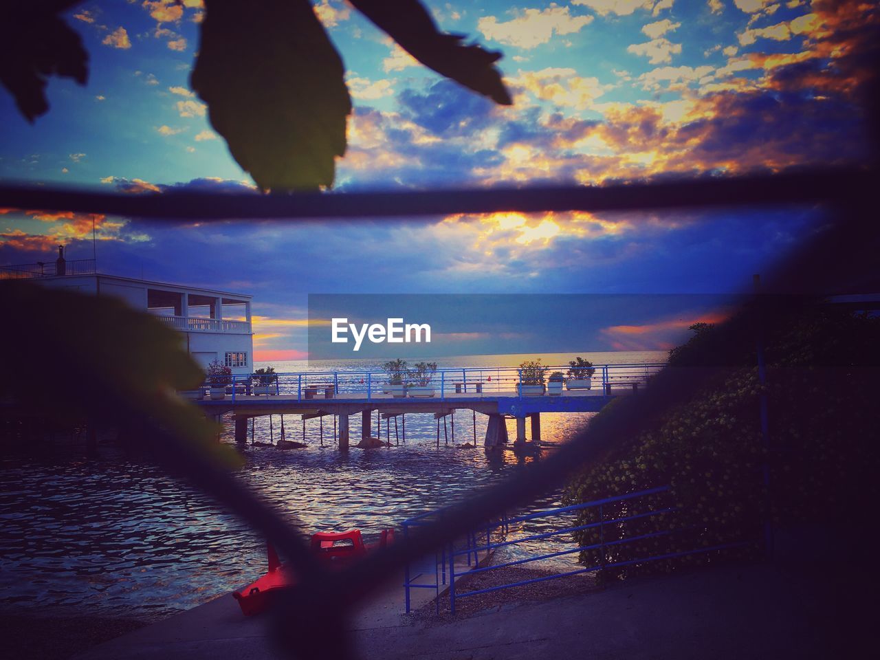 Pier over sea against cloudy sky during sunset seen through fence