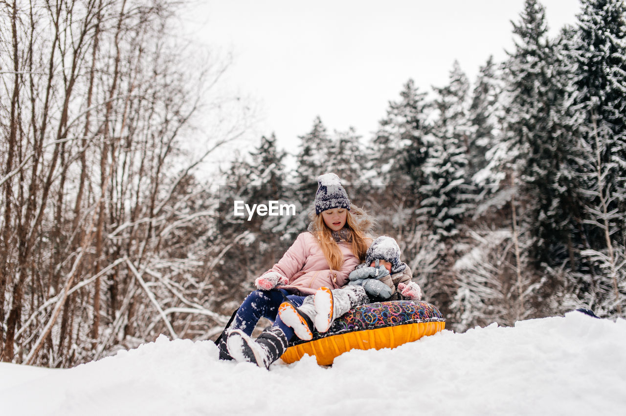 Brother and sister are sitting in a tubing in the snow and riding downhill