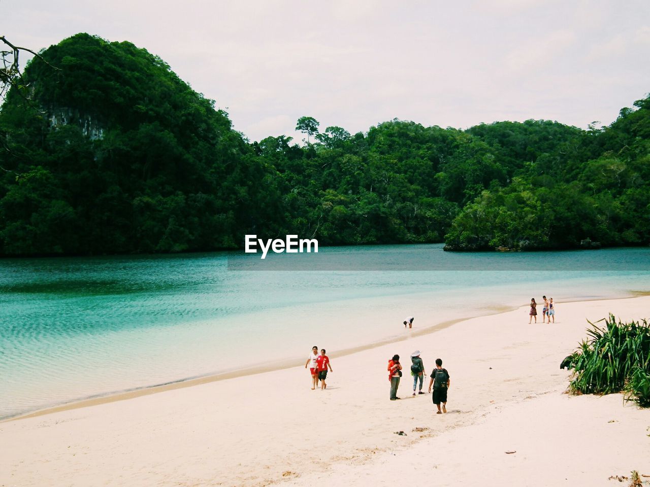 People walking on beach by sea against cloudy sky