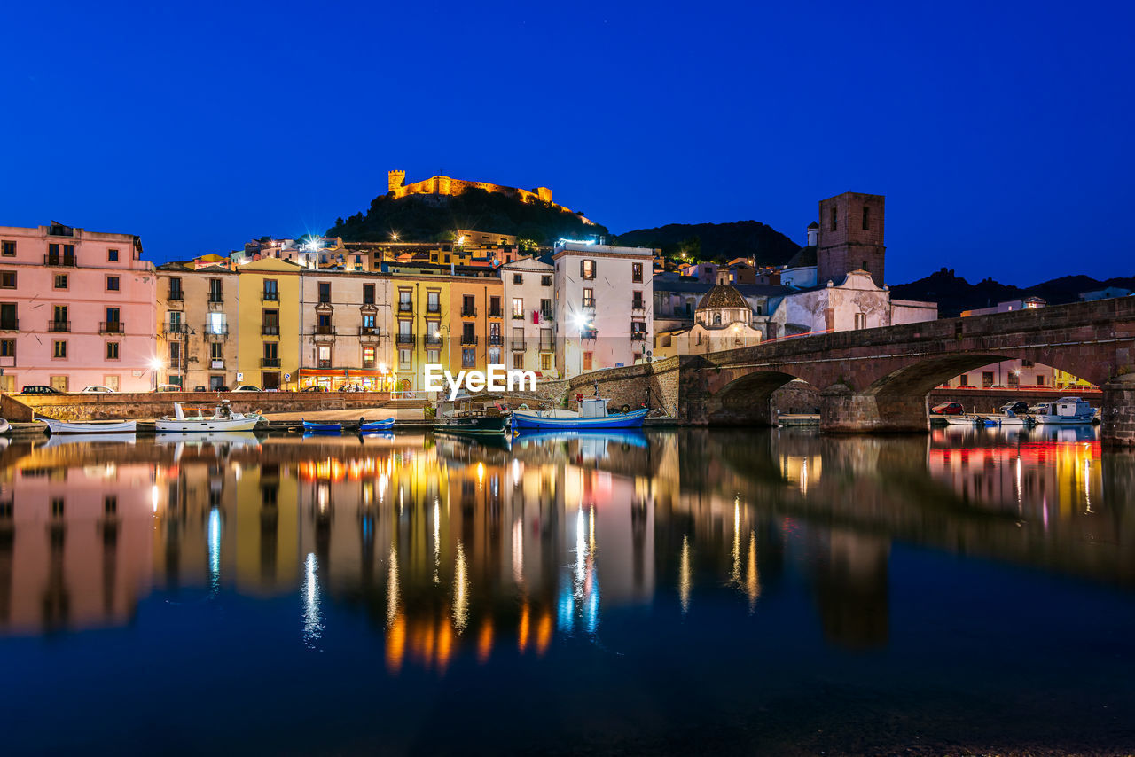 RIVER BY ILLUMINATED BUILDINGS AGAINST CLEAR SKY AT DUSK