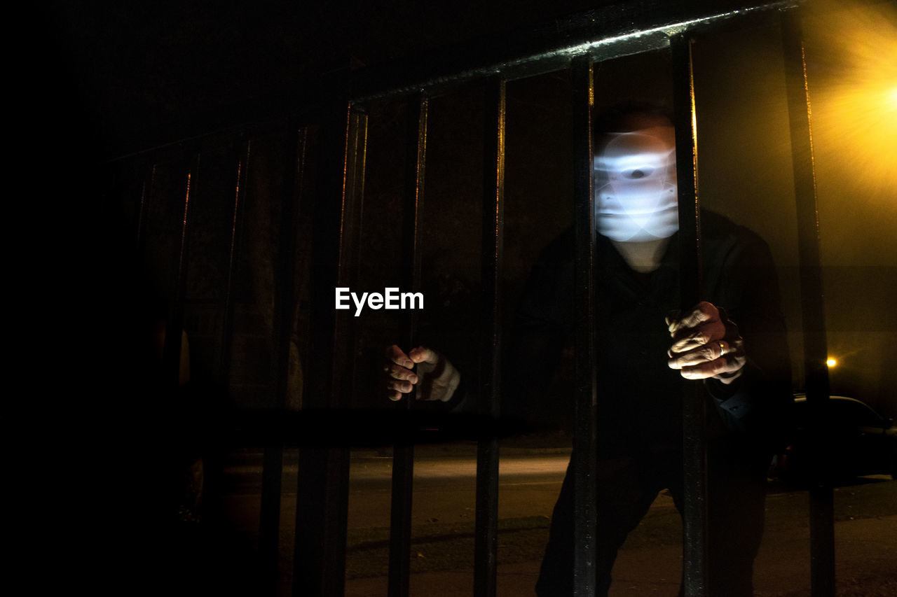 Man wearing mask holding gate outdoors at night