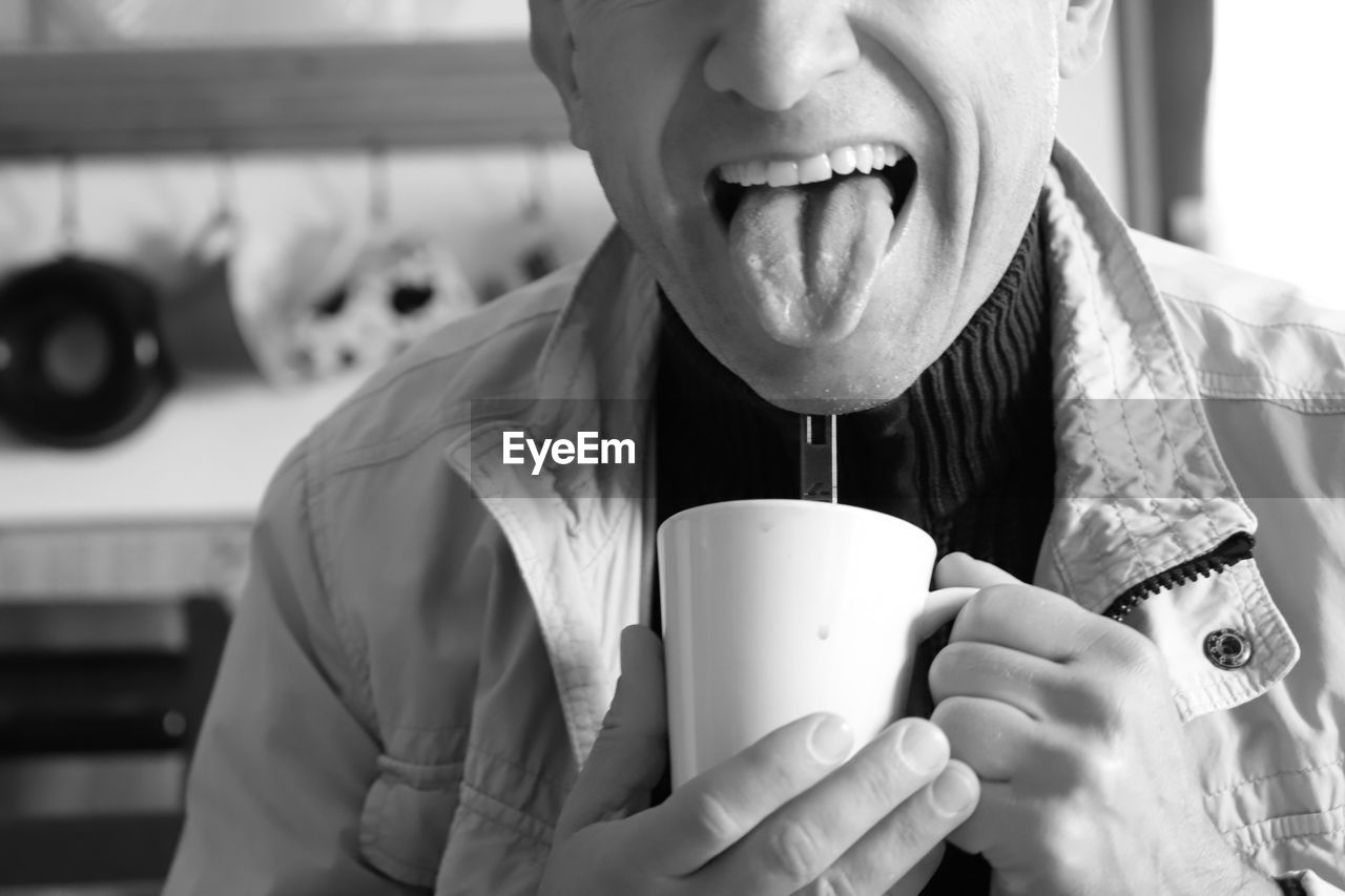 Midsection of man sticking out tongue while having coffee in cup