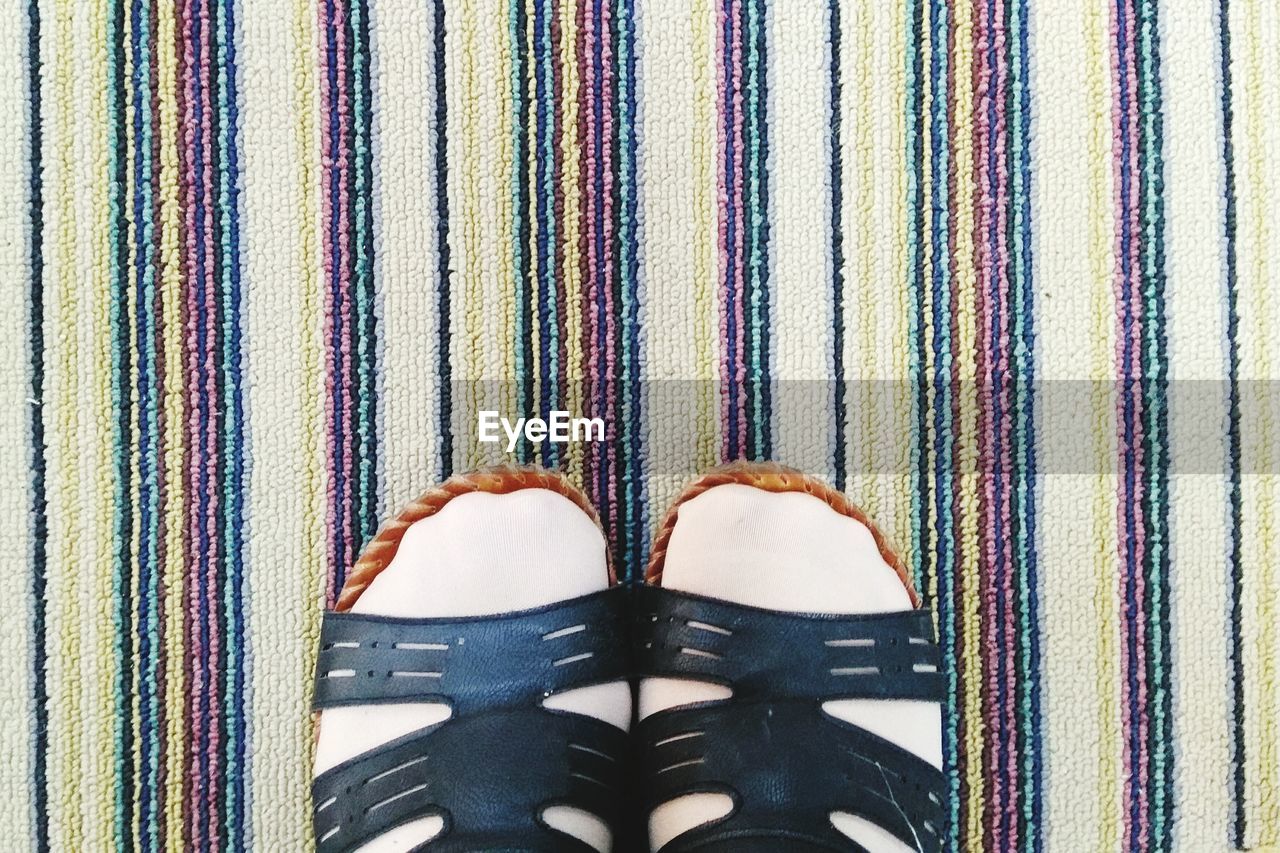 Low section of person wearing sandals while standing on carpet